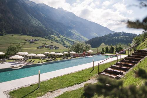 a pool with chairs and umbrellas next to a mountain at Hotel Sonklarhof in Ridanna