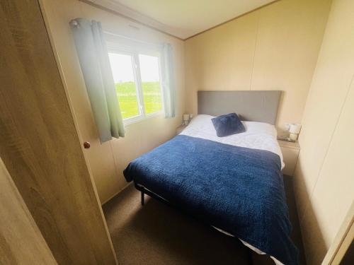 a bedroom with a bed with a blue blanket and a window at The Pastures Holiday Lodge in Tattershall