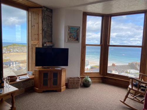 sala de estar con TV de pantalla plana y ventanas grandes. en HUER'S WATCH a beautifully presented PRIVATE APARTMENT with far reaching VIEWS Over ST IVES HARBOUR and BAY and FREE ONSITE PARKING for LARGER GROUPS book along with our Connecting TWO SISTER APARTMENTS, en St Ives
