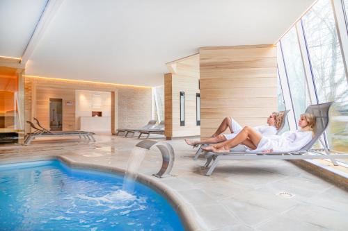 two women sitting in chairs next to a swimming pool at Hotel Donny in De Panne