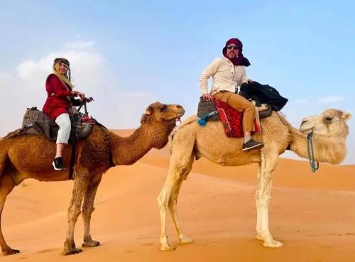 two people riding on the backs of camels in the desert at Merzouga Luxurious Camp in Merzouga