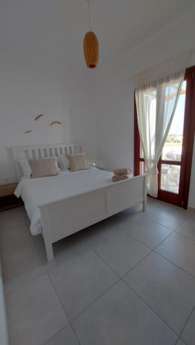 a white bedroom with a white bed and a window at Sea breeze houses in Monolithos