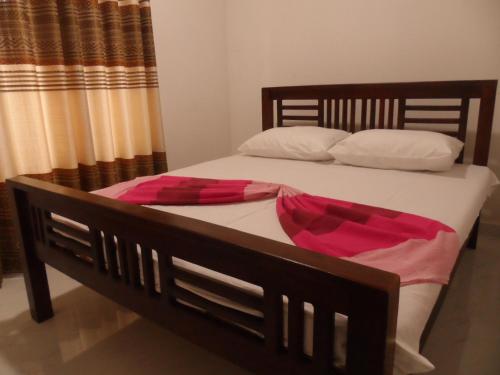 ein Holzbett mit weißer und rosa Bettwäsche und Kissen in der Unterkunft D2 Holiday Inn in Badulla