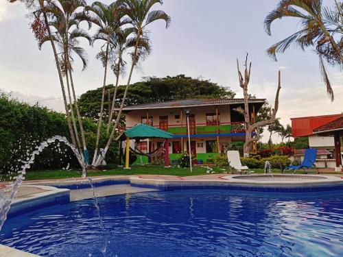 une piscine en face d'une maison avec des palmiers dans l'établissement Finca Hotel Amanecer del Cafeto, à Montenegro