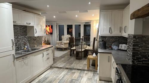 a kitchen with white cabinets and a living room at Five Farthings Stylish cottage in Littleworth