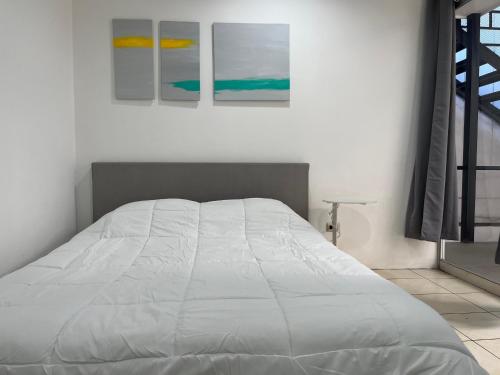 SJO Oasis Hostel في سان خوسيه: سرير ابيض في غرفة نوم يوجد ثلاث لوحات على الحائط