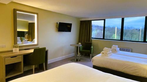a hotel room with two beds and a desk and a mirror at Hellidon Lakes Hotel in Daventry
