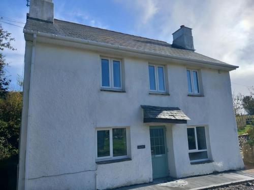 a white house with a green door and windows at Rural Cornish farmhouse in Liskeard