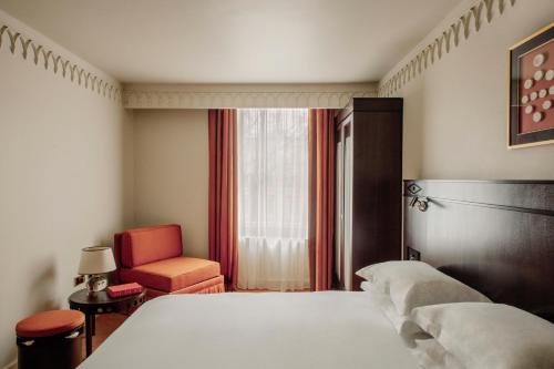 a bedroom with a bed and a chair and a window at Grand Hotel Bellevue London in London