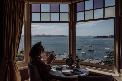 a woman sitting at a table reading a book looking out a window at Grande Vue in Hobart