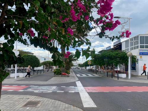 una calle de la ciudad con flores rosas y edificios en Habitaciones privadas cerca de la playa y aeropuerto en casa compartida con otros huéspedes, en Playa Honda