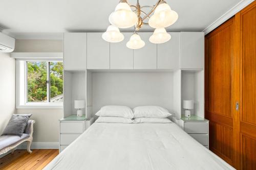 a white bedroom with a large bed and a chandelier at Elegant 1-Bed with Study by Balmain Wharf in Sydney