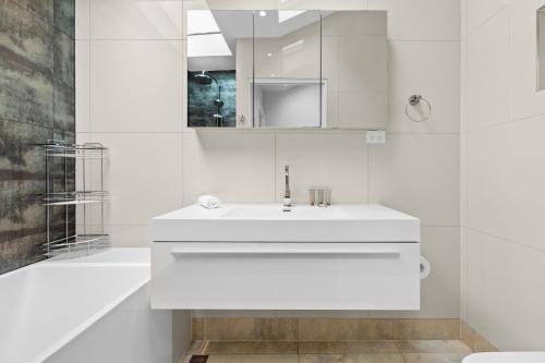 La salle de bains blanche est pourvue d'un lavabo et d'une baignoire. dans l'établissement Elegant 1-Bed with Study by Balmain Wharf, à Sydney