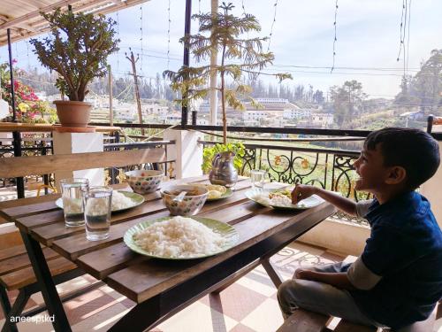 un joven sentado en una mesa de madera con platos de comida en SNR Cottage & Rooms en Ooty