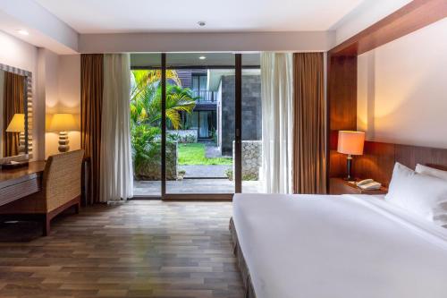 a bedroom with a bed and a desk and a large window at Le Grande Bali in Uluwatu