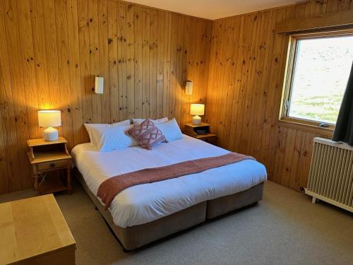 een slaapkamer met een bed met houten wanden en een raam bij Peer Gynt Ski Lodge in Perisher Valley