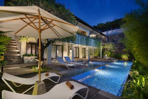 an outdoor patio with an umbrella and chairs and a pool at AmantraNa Canggu in Canggu