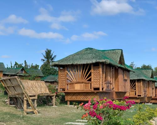 a wooden hut with a grass roof and flowers at PAPABO Adventure Village in Moalboal