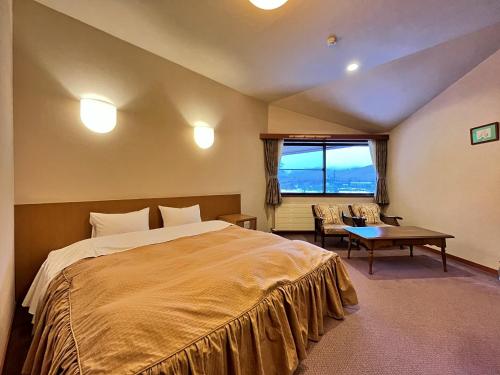 a bedroom with a bed and a table and a window at ペンション湖風 in Tateshina