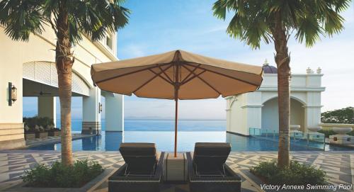 patio z 2 krzesłami i parasolem w obiekcie Eastern & Oriental Hotel w mieście George Town