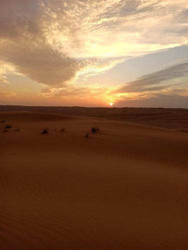 a sunset in the desert with the sun setting at Endless Dunes Camp in Bidiyah