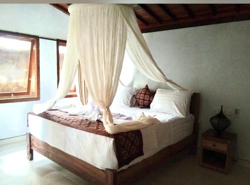ein Schlafzimmer mit einem Himmelbett mit weißer Bettwäsche und Kissen in der Unterkunft Belvilla 93800 The Abhinaya Villa Near Central Ubud in Payangan