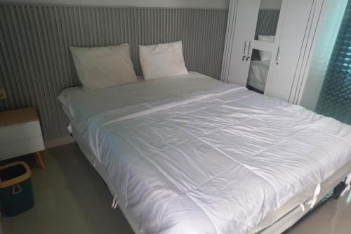 Elle comprend un grand lit blanc avec des draps et des oreillers blancs. dans l'établissement Capital O 93816 Cerry Village, à Tegal