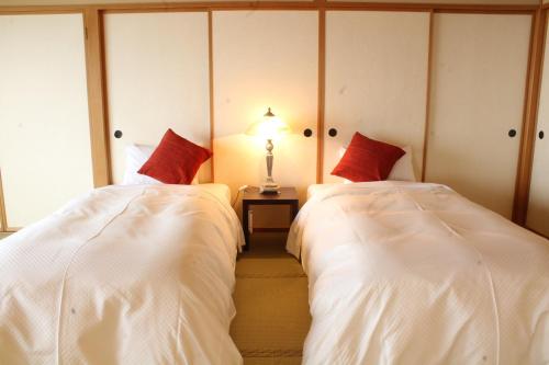 a bedroom with two beds with white sheets and red pillows at Hotel Symphony Annex Sagae Onsen in Sagae
