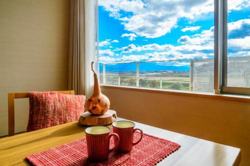 a table with two cups and a vase on a table with a window at Hotel Symphony Annex Sagae Onsen in Sagae