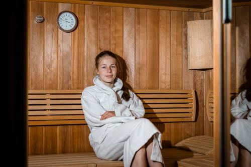 a girl sitting on a bench in a room with a clock at Familienbauernhof Glawischnig-Hofer in Gmünd in Kärnten