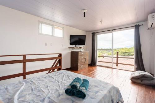 ein Schlafzimmer mit einem Bett mit Fernseher und einem Balkon in der Unterkunft Flat Romântico da Guarda do Embaú SC in Palhoça