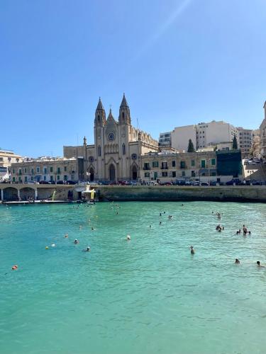 people swimming in the water in front of a building at Malta Crown guesthouse in St Julian's