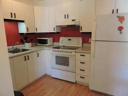 a kitchen with white cabinets and a white refrigerator at Appartement touristique #5 Immeuble MH in LʼAnse-Saint-Jean