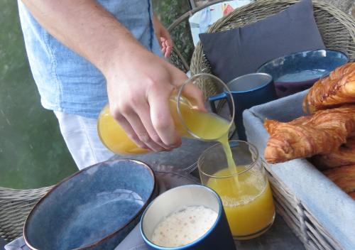 a person is pouring orange juice into a glass at Domaine La Synchronicité - Gîte et Chambres d'Hôtes in Vaudrimesnil