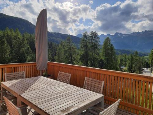 una terraza de madera con mesa y sombrilla en Chesa Vista Mezdi 6 Bergbahnen Sommer und ÖV inklusive en Pontresina
