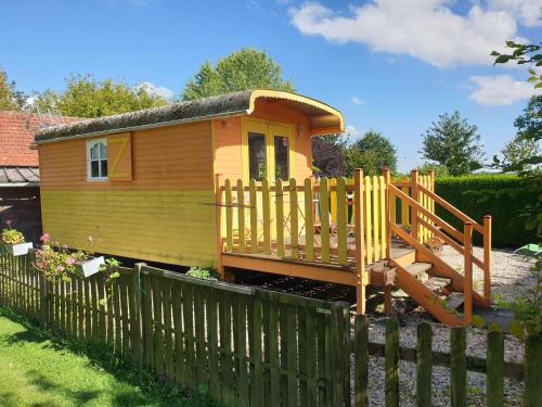 ein kleines gelbes Haus mit einem Holzzaun in der Unterkunft La roulotte du bois du fil in Vassonville