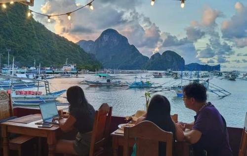 a group of people sitting at a table near the water at La Salangane Beach Hotel - Downtown in El Nido