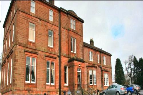 un edificio de ladrillo con coches estacionados frente a él en OYO Kirkconnel Hall Hotel, en Ecclefechan