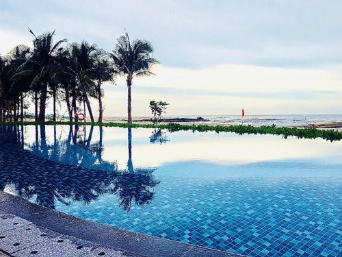 a swimming pool next to the ocean with palm trees at Hồ Tràm Wonderland - Mocha Villa 2 Phòng Ngủ in Ho Tram