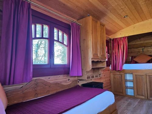 パディラックにあるLes Roulottes du Petit Gouffre de Padiracの紫色のカーテンが付いたベッドルーム1室、キャビン内のベッド1台