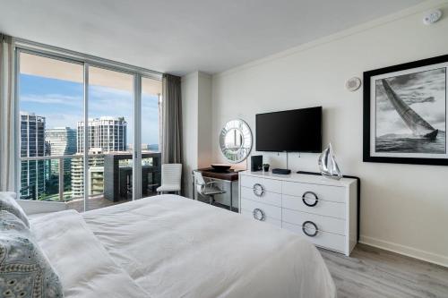 a white bedroom with a bed and a television at City View Balcony steps from Restaurants, Peacock Park & Marina in Miami