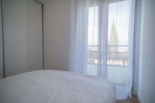 um quarto com uma cama branca e uma grande janela em GuestReady - Elegant nature escape in vibrant Nice em Nice