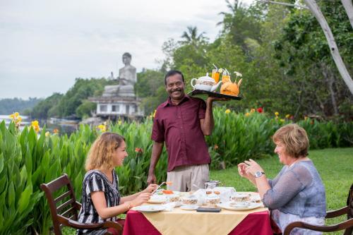 three people sitting around a table with a man holding a tray of food at AIDA Hotel - Bentota in Bentota
