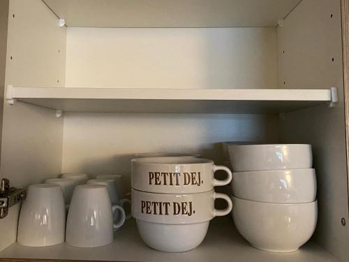 a cupboard filled with white mugs sitting on a shelf at APPART - T3 - 6 PERSONNES – GOLF CAP D’AGDE in Cap d'Agde