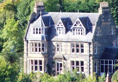 a large stone house with trees in the background at The Retreat Hotel in Strathpeffer