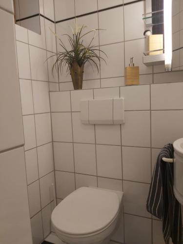a white tiled bathroom with a toilet and a plant at Waldwinkel in Treuchtlingen