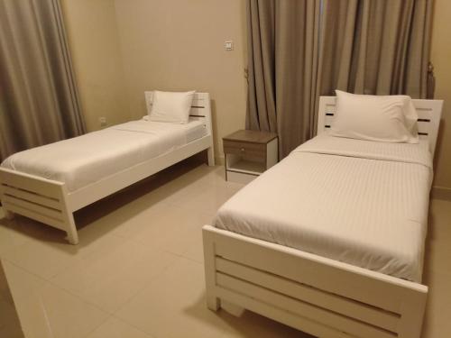 Star Dubai Apartment في صلالة: سريرين في غرفة ذات أغطية ووسائد بيضاء