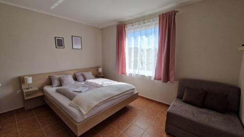 a bedroom with a bed and a chair and a window at Silence Apartmanház Zalakaros in Zalakaros