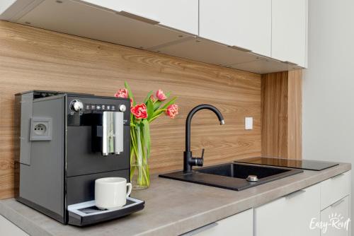 eine Küche mit einem Waschbecken, einer Kaffeemaschine und Blumen in der Unterkunft Grunwaldzka 12 D13 - Easy-Rent Apartments 50m od plaży in Pobierowo