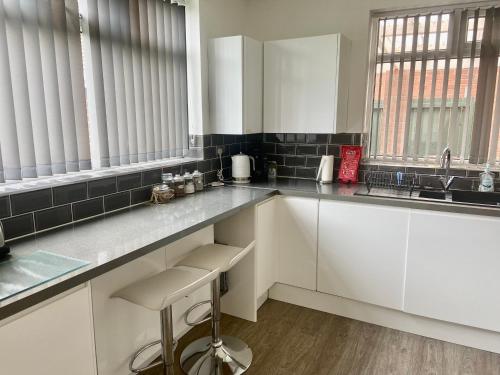 a kitchen with white cabinets and a bar stool at BeRo Bungalow with a hot tub & a large garden! in Withernsea